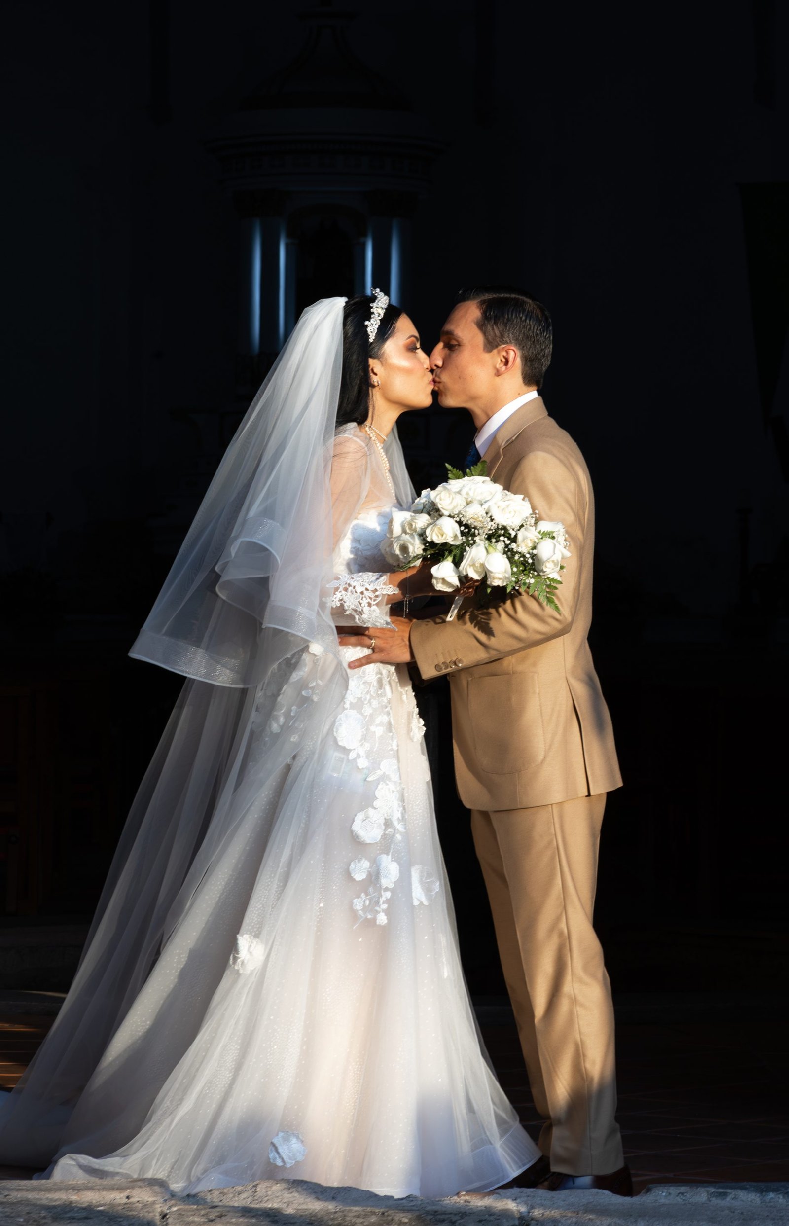 Novios besándose iluminados contra el interior oscuro de una iglesia