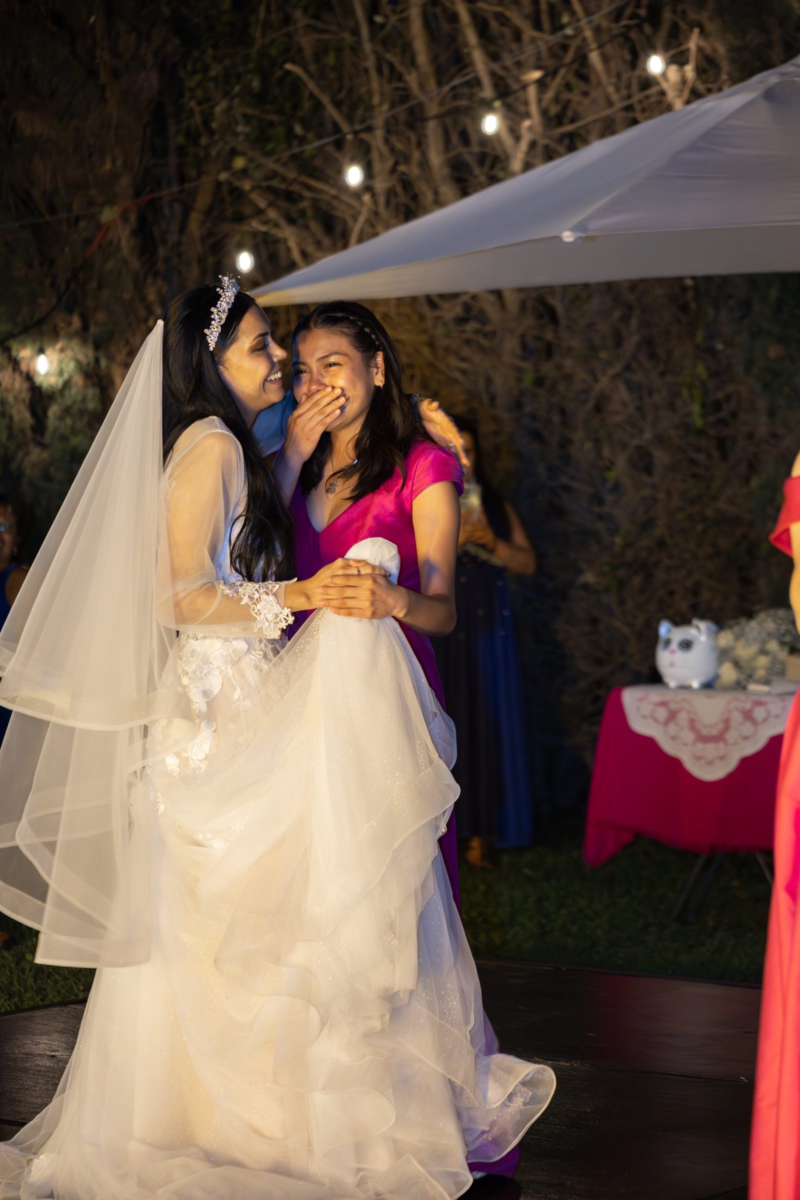 Novia abrazando a una invitada que se cubre la boca, emocionada